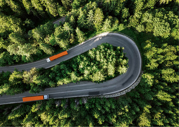 Aerial view of winding road in high mountain pass trough dense green pine woods 